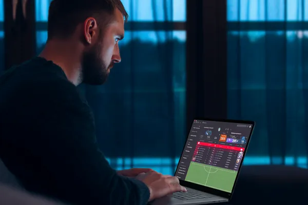 PJOK Mobile App — Your complete hub for casino and sports A man focused on his laptop with live stats in the background, highlighting the dedicated sports and gaming features of the PJOK mobile app.